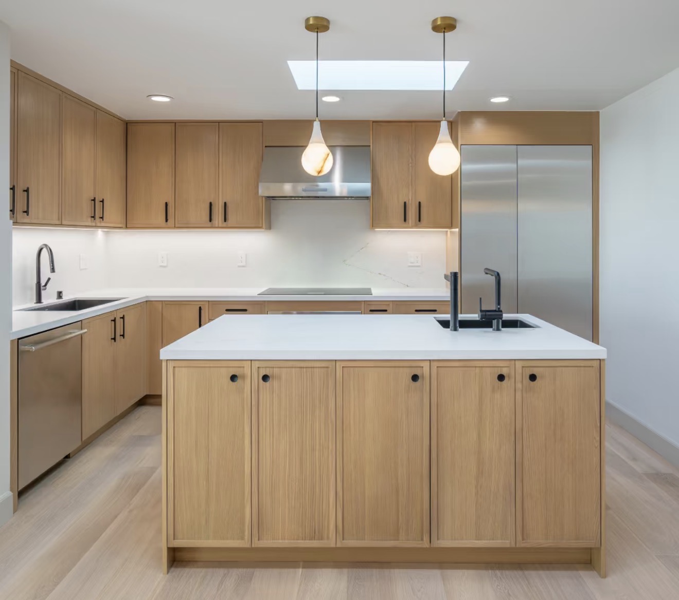 Slim oak Shaker kitchen and island with white countertops, black fixtures and pendant lights